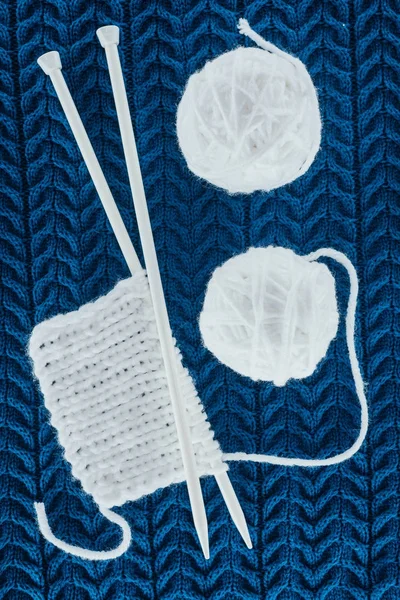 Top view of white yarn balls and knitting needles on blue knit — Stock Photo