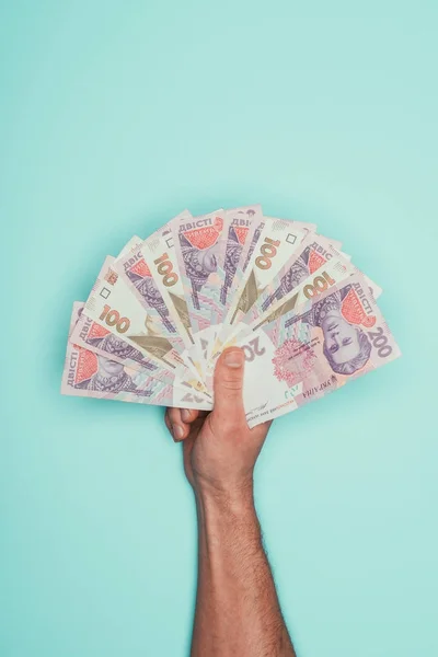 Cropped shot of man holding bunch of ukrainian cash isolated on turquoise — Stock Photo