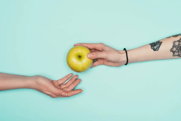 Cropped shot of women passing fresh apple isolated on turquoise — Stock Photo