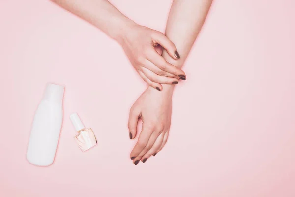 Cropped shot of woman with nail polish and bottle of lotion isolated on pink — Stock Photo