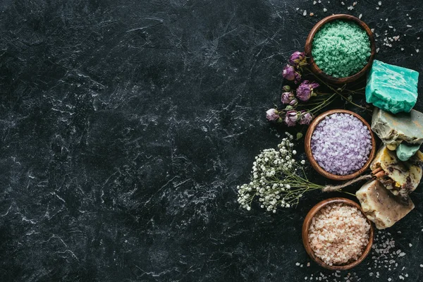 Flat lay with homemade soap, dried flowers and sea salt in wooden bowls on black marble surface, spa concept — Stock Photo