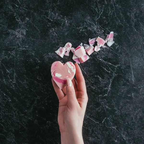 Vista ritagliata della mano femminile con sapone a forma di cuore rosa sulla superficie di marmo nero — Foto stock