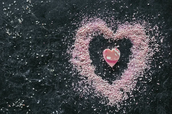 Top view of pink heart shaped soap and sea salt on black marble surface, spa concept — Stock Photo