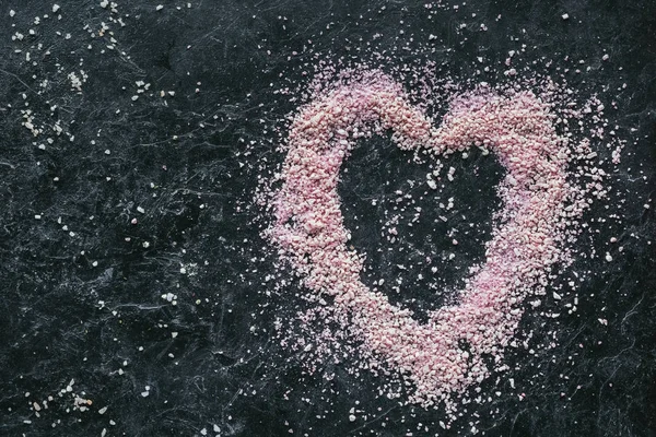Vista superior de la sal de mar rosa en forma de corazón para spa en la superficie de mármol negro - foto de stock