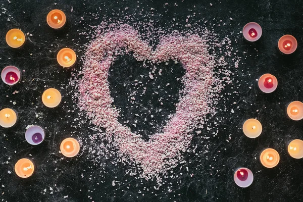 Top view of heart shaped pink sea salt and candles on black marble surface, aroma therapy concept — Stock Photo