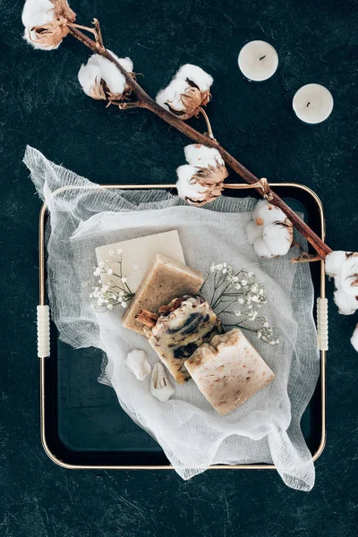 Couche plate avec du savon naturel fait maison et des fleurs de coton séchées sur gaze dans un plateau — Photo de stock