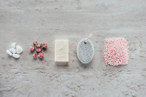 Vista superior de piedras, rosas secas, jabón natural, piedra pómez y sal himalaya para spa en superficie de mármol - foto de stock