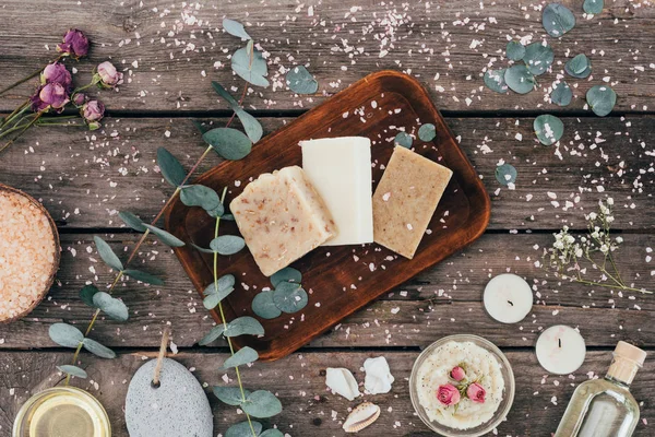 Top view of homemade natural soap, eucalyptus, spa treatment and salt on wooden board — Stock Photo