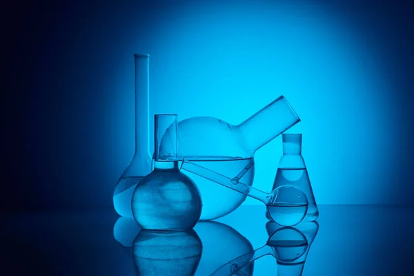 Different glass flasks on reflecting table in laboratory on blue — Stock Photo