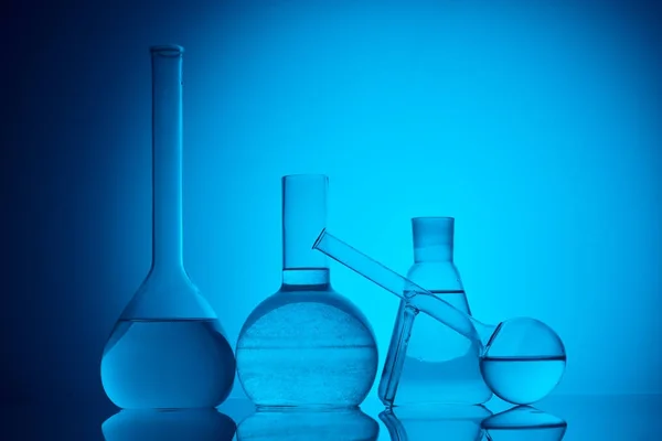 Diferentes frascos de vidrio con líquido para ensayo químico en azul - foto de stock