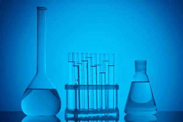 Glass tubes on stand and glass flasks with liquid on table on blue — Stock Photo