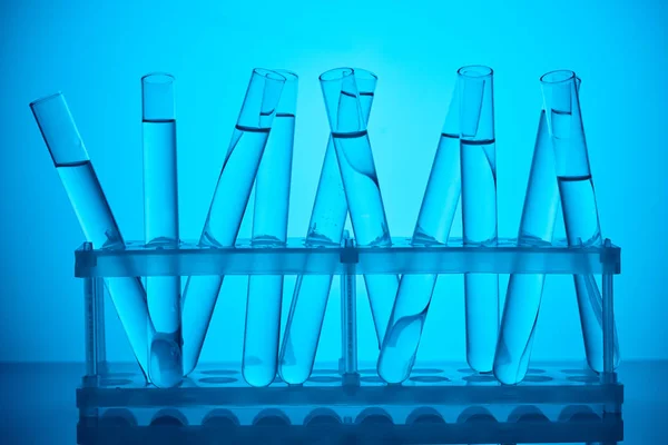 Tubes en verre avec liquide sur pied pour analyse scientifique sur bleu — Photo de stock