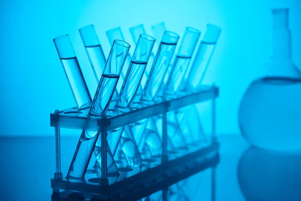 Tubi di vetro con liquido sul supporto per analisi chimiche in laboratorio su blu — Foto stock