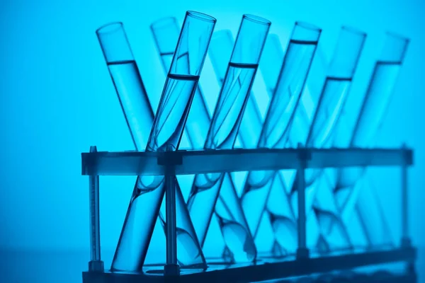 Tubos de vidrio con líquido sobre soporte en laboratorio sobre azul - foto de stock