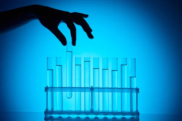 Cropped image of chemist taking glass tube from stand on blue — Stock Photo