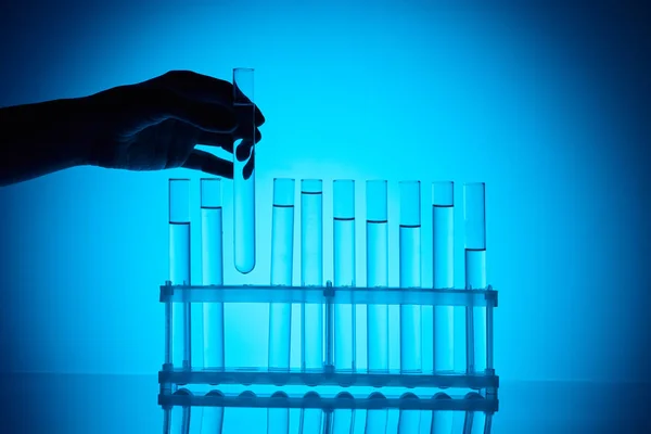 Imagen recortada de farmacia femenina tomando tubo de vidrio de pie en azul - foto de stock