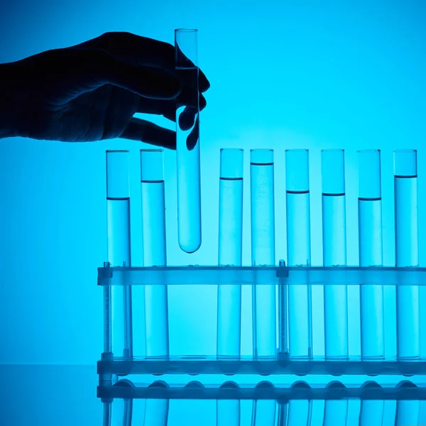 Cropped image of female chemist taking glass tube with substance from stand on blue — Stock Photo