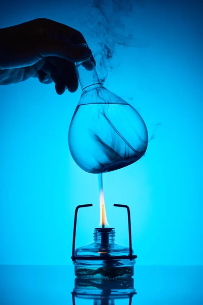 Cropped image of chemist warming up substance for analysis on blue — Stock Photo