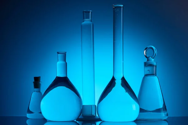 Different glass flasks with liquid in chemical laboratory on blue — Stock Photo