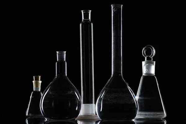 Transparent glass flasks with substance in laboratory on black — Stock Photo