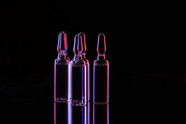 Ampoules en verre transparent avec liquide sur la table sur noir — Photo de stock