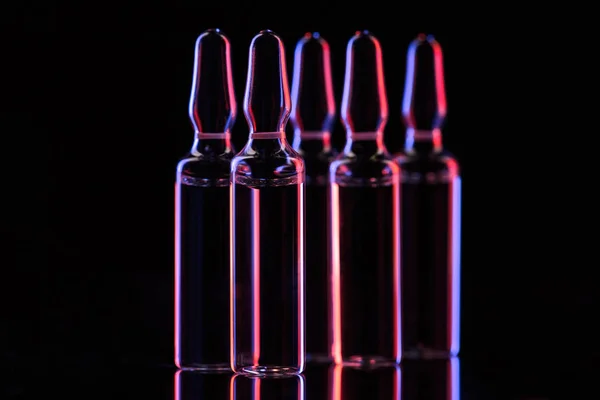 Transparent glass ampoules with liquid and reflection on table on black — Stock Photo