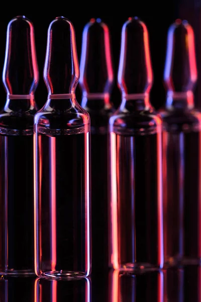 Close up view of transparent glass ampoules with liquid on table on black — Stock Photo