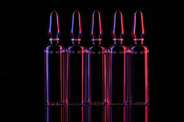 Row of transparent glass ampoules with liquid on table on black — Stock Photo