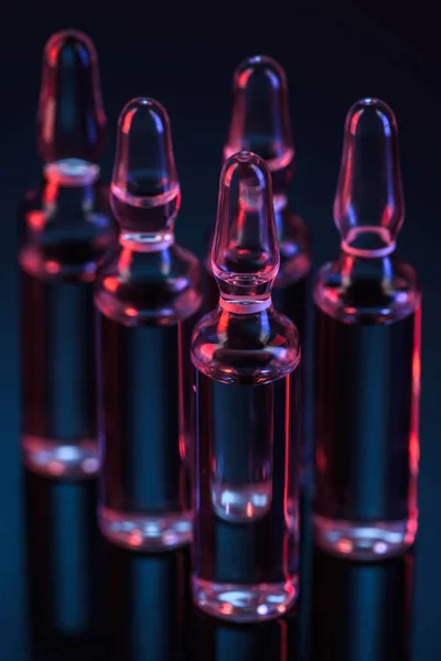Close up of five transparent glass ampoules with liquid on table on black — Stock Photo