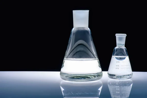 Glaskolben mit Flüssigkeit auf weißem Tisch auf schwarzem — Stockfoto