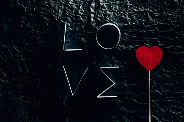 Word LOVE made of paper stripes with heart on stick on black concrete surface — Stock Photo