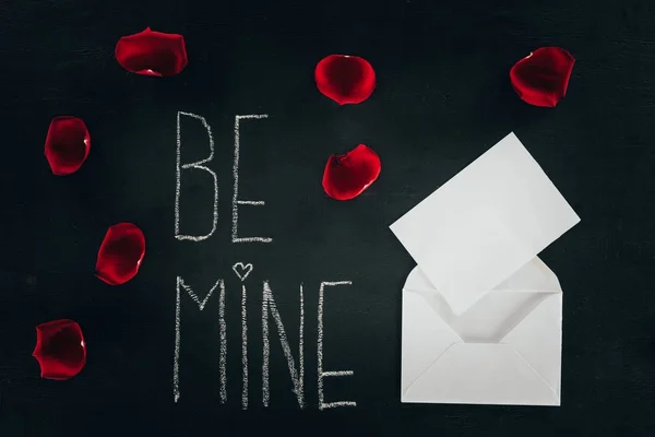 Lettering BE MINE surrounded with rose petals and envelope on black surface, st valentines day concept — Stock Photo