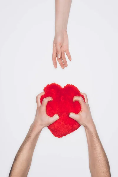 Colpo ritagliato di uomo spremendo cuscino cuore rosso, mentre la donna che raggiunge per esso isolato su bianco — Foto stock