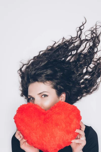 Jovem mulher cobrindo rosto com travesseiro em forma de coração isolado no branco — Fotografia de Stock