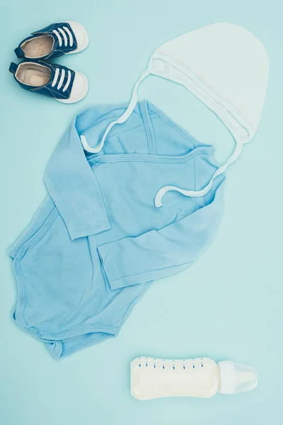 Vue de dessus des vêtements bébé et biberon de lait isolé sur bleu — Photo de stock