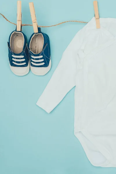 Top view of baby bodysuit and shoes drying on rope isolated on blue — Stock Photo