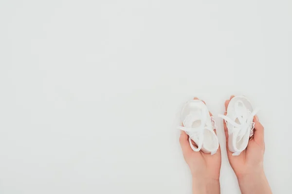 Imagen recortada de mujer sosteniendo zapatos de bebé blancos aislados en blanco - foto de stock