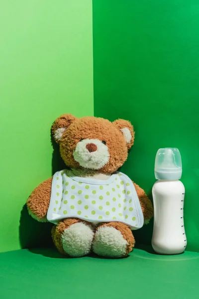 Teddy bear and baby bottle with milk on green — Stock Photo