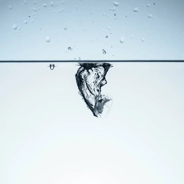 Cubo de hielo en agua con salpicadura, aislado en blanco - foto de stock