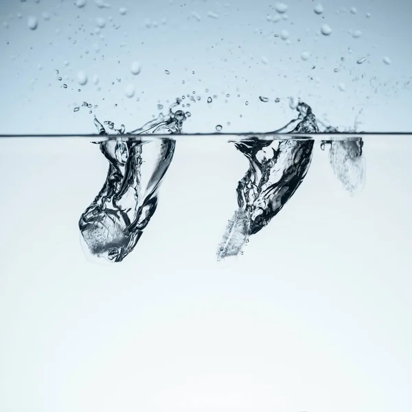 Cubitos de hielo en agua con salpicaduras, aislados en blanco - foto de stock