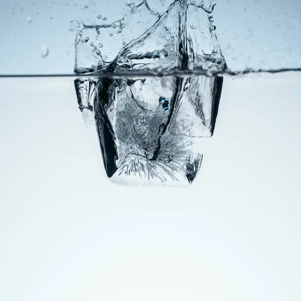 Ice cube in water with splash, isolated on white — Stock Photo