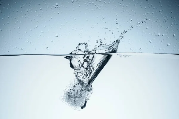 Cubo de hielo en agua con salpicaduras y gotas, aislado en blanco - foto de stock