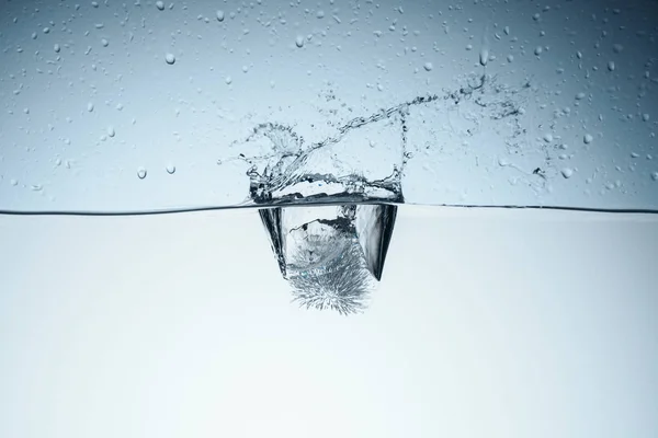 Cubo de hielo en agua con salpicaduras y gotas, aislado en blanco - foto de stock