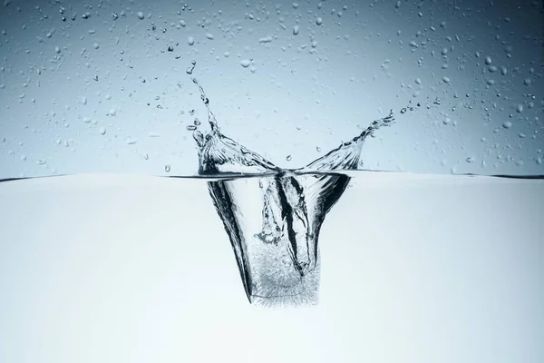 Cubo de hielo en agua con salpicaduras y gotas, aislado en blanco - foto de stock
