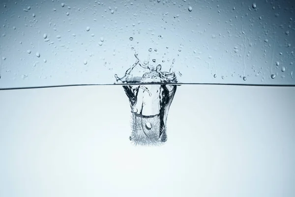 Cubo de hielo salpicando en el agua, aislado en blanco - foto de stock