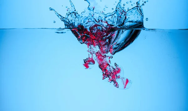 Ice cubes with berries in water with splashes and drops, isolated on blue — Stock Photo