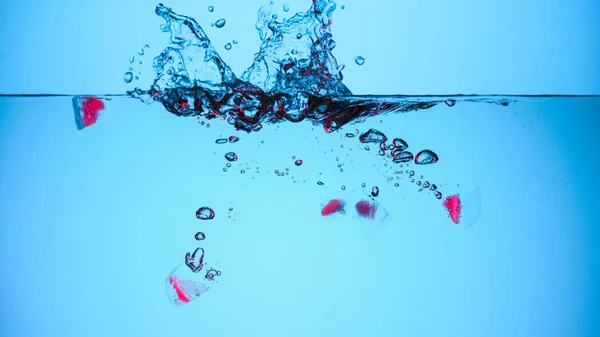 Eiswürfel mit Kirschen in Wasser mit Spritzern, isoliert auf blau — Stockfoto