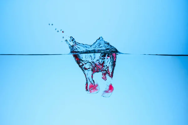 Eiswürfel mit Beeren in Wasser mit Spritzwasser, isoliert auf blau — Stockfoto