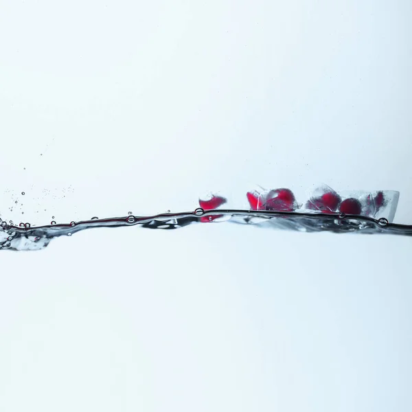 Cubetti di ghiaccio con bacche rosse che si sciolgono in acqua, isolati su bianco — Foto stock