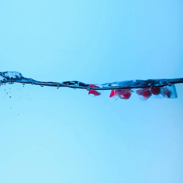 Ice cubes with pink berries in water with bubbles, isolated on blue — Stock Photo